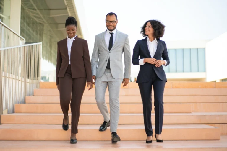 3 Personen in Business-Kleidung gehen auf dem Weg zum Career Transition Coaching fr?hlich eine Treppe hinunter.